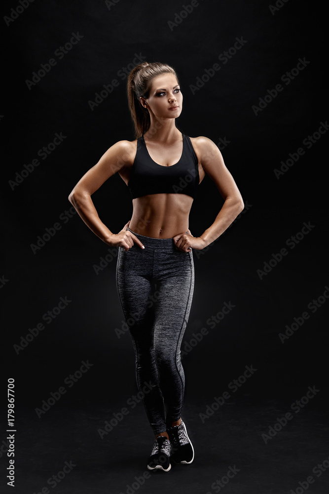 Shot of a strong woman with muscular abdomen in sportswear. Fitness female model posing on black background.