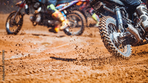 Details of flying debris during an acceleration with mountain bikes race in dirt track in sunshine day time in blurry background. Concept of focus between an accelerate in action sport