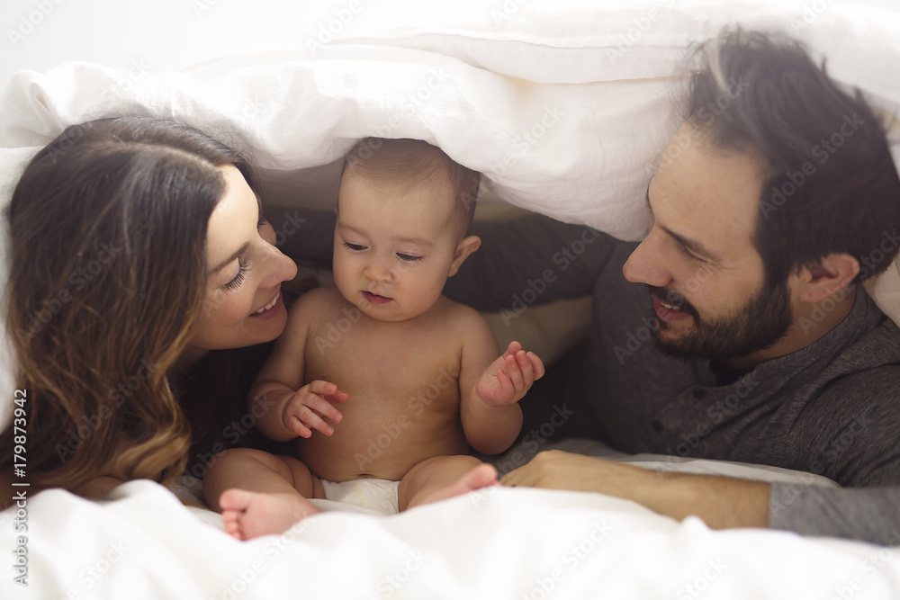 Couple enjoying with baby under blanket on bed at home Couple enjoying with baby under blanket on bed at home