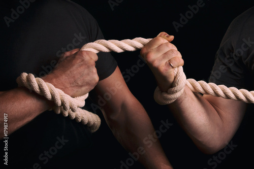 Tug-of-war. Men tighten a rope on a black background