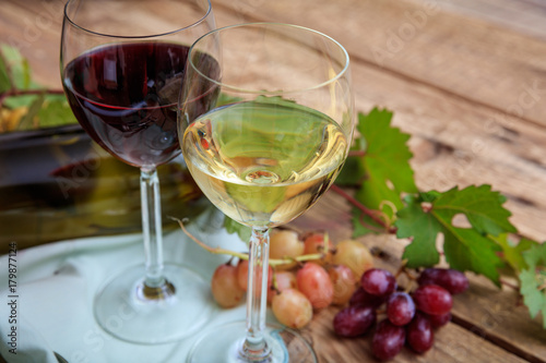 Red and white wine glasses and fresh grapes on wooden background