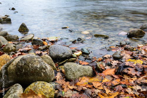 Steine im Wasser mit orangen laubglätter am Ufer