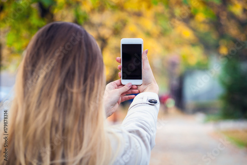 Woman taking picture with smartphone in colorful autumn street
