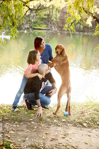 Happy family of father, mother and daughter on the riverside playing with their dog. Animal lovers