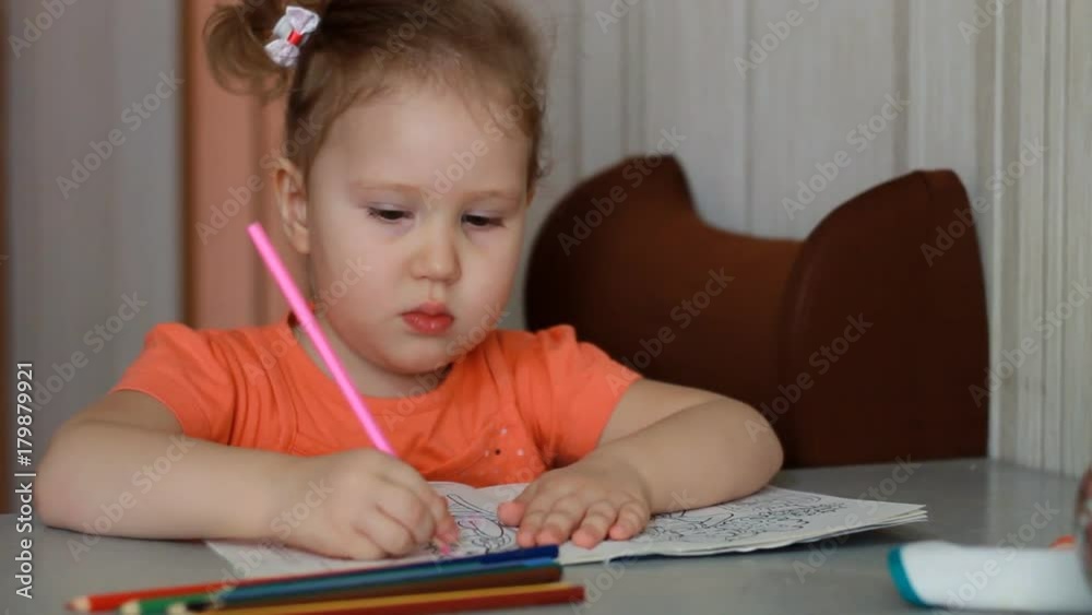 An amusing pretty girl sits at a table and draws in multicolored pencils. Child and creativity. An amusing pretty girl sits at a table and draws in multicolored pencils. Child and creativity.