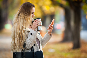 Beautiful woman using smartphone walking colorful autumn street