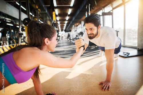 Young handsome fitness couple smiling and holding hands each other while doing push ups together in the gym.