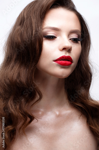 A young girl with a Hollywood wave and classic makeup. Beautiful model with red lips and arrows on eyes. Evening makeup and hairstyle. Beauty of the face. White isolated background. Shining skin.