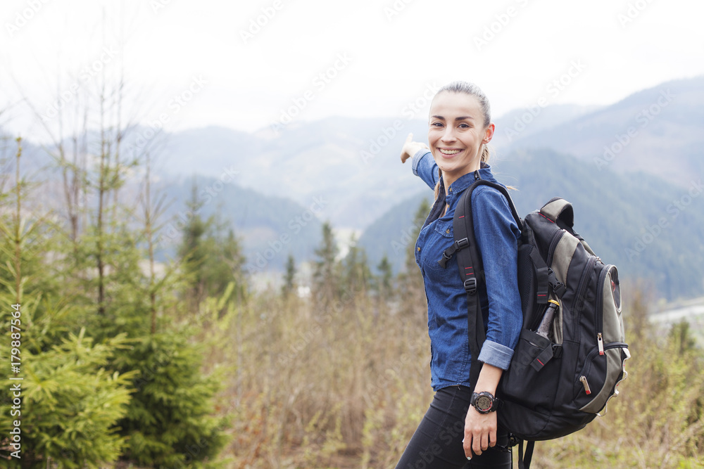 Young smiling tourist woman with a backpack in the mountains enjoying the scenery