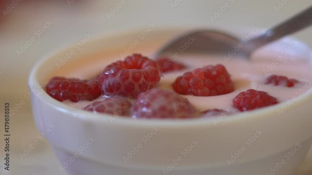 large juicy berries of raspberries fall in a plate with white yogurt. delayed shooting. large salty berry appetizingly lie on the surface. A small teaspoon slowly raises and lowers fresh berries. a