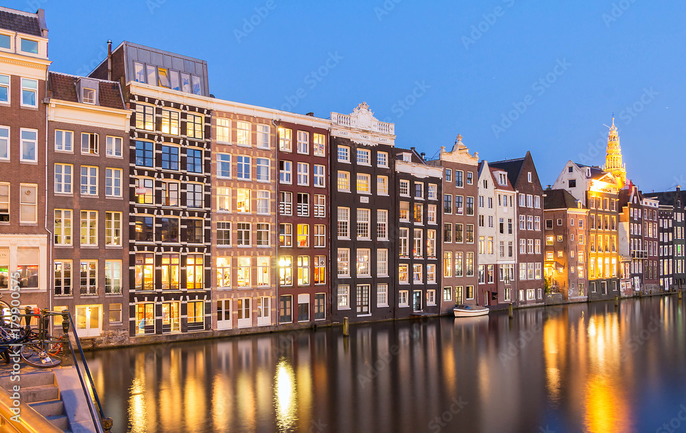 Houses facades over canal with reflections illuminated at night, Amsterdam.