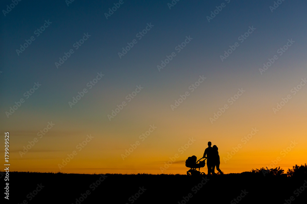 Sillhouette of a young couple walking during sunset with a baby in the stroller