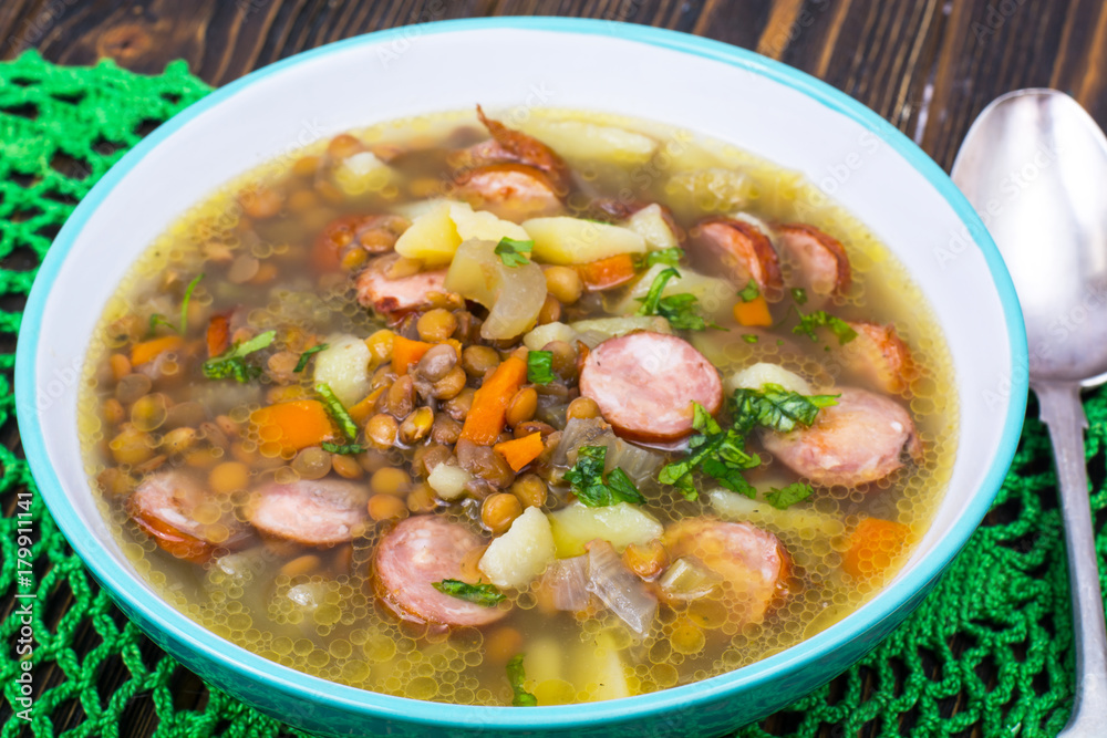 Soup with lentils, celery and sausages on old wooden table Soup with lentils, celery and sausages on old wooden table