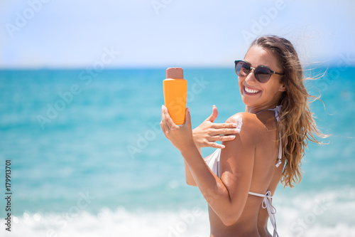 Beautiful girl in bikini applying sunscreen cream on the beach