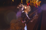 Positive Caucasian Woman In Leather Jacket and Blue Jeans Playing on Rails With Bag Outdoors at Night.Playing the Guitar with Expression. Halogen and Flash Lights are Used.