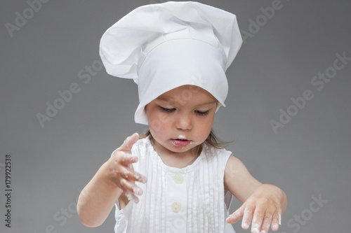 Cooking Ideas. Portrait of Caucasian Little Girl in Cook Uniform Posing with Smudgy Face Against Gray Background.