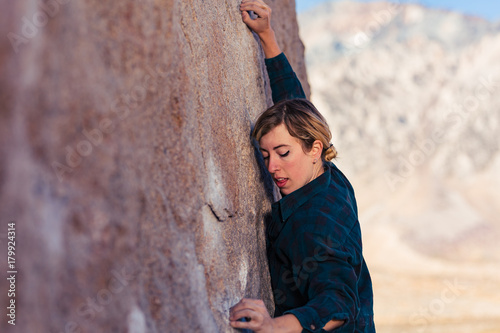 Thin blonde caucasian woman wearing flannel against the cold rock climbing on boulders in the desert of California