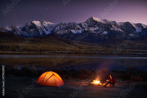 Man tourists sitting in the illuminated tent near campfire