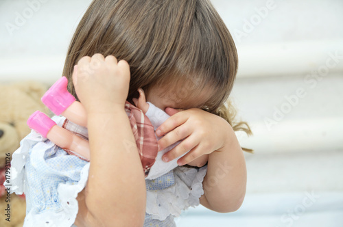 Little girl with doll playful hiding crying