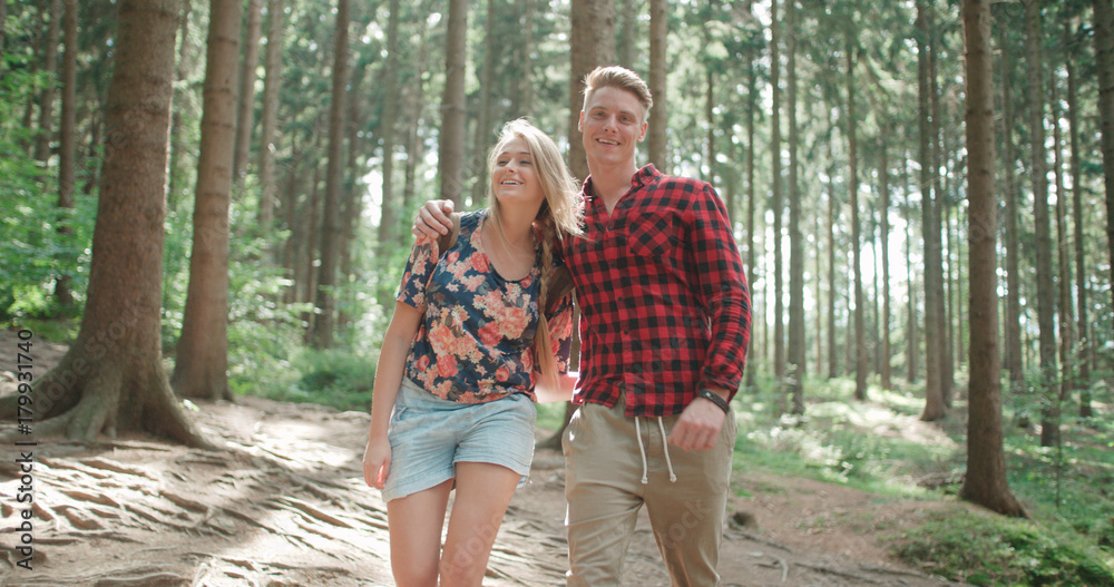 Portrait of beautiful caucasian couple spending time in a forest during sunny day. Smiling couple  relaxing in woods.