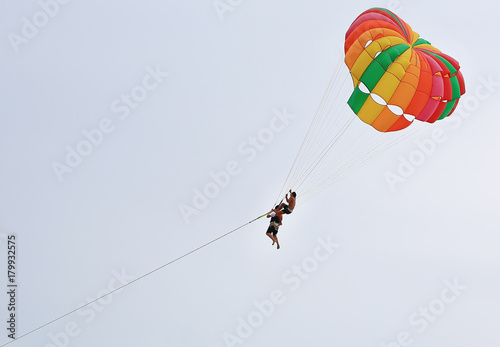 People are enjoy parasailing water sport. Close up fly with colorful parachute on the sky over the beach.