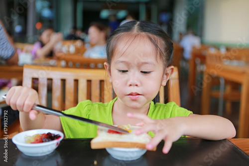 Cute little Asian girl eating bread sheet. Asian girl having breakfast.