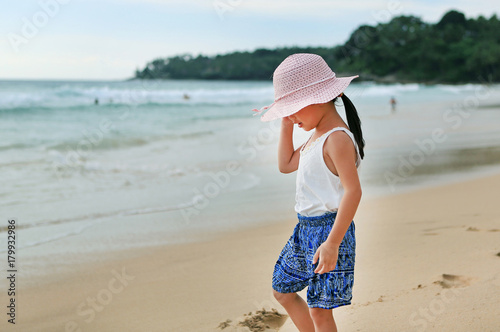 Little asian girl wear straw hat walking on the beach.