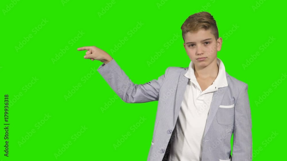 Adorable boy in suit point with finger on something at chroma key background
