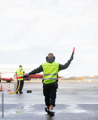 Ground Crew Signaling To Airplane Against Sky