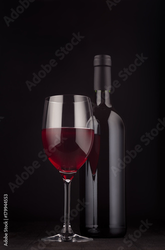 Bottle of red wine and wine glass mock up on elegant dark black wooden background, vertical. Template for portfolio, advertising, design, branding identity, cover magazine, bar and restaurant menu.