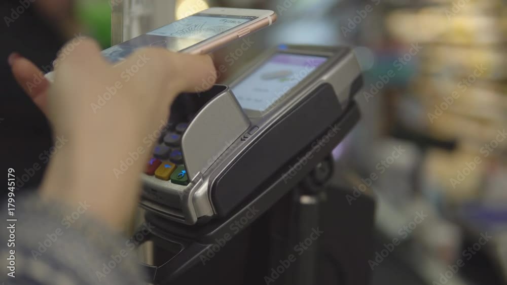 Girl buying food and paying with his phone. Wireless payment concept. Supermarket store