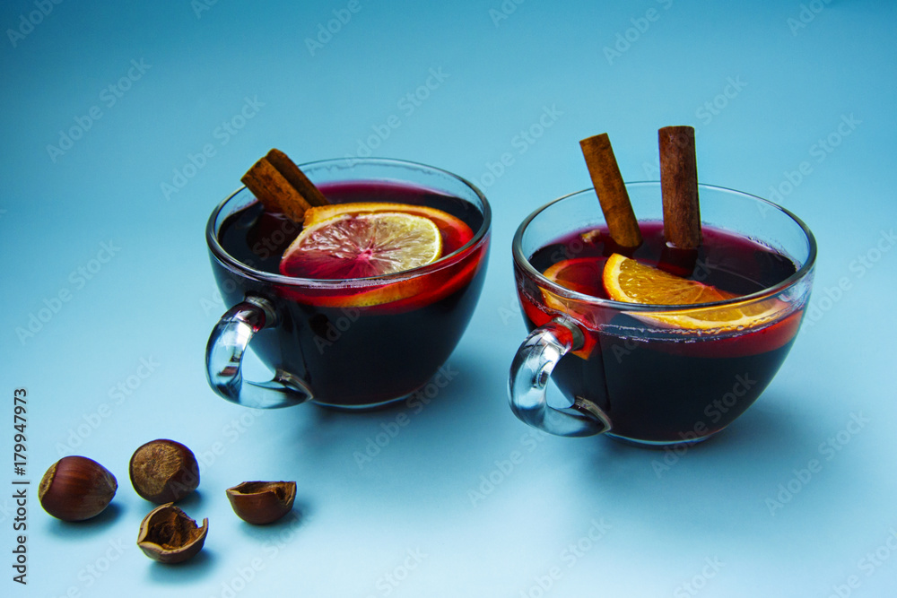 Two glass cups of mulled wine with nuts on a bright blue background. Two glass cups of mulled wine with nuts on a bright blue background.