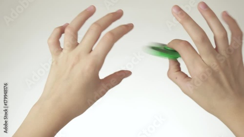 Hands of a teenage girl spin a green fidget spinner on white background stock footage video photo