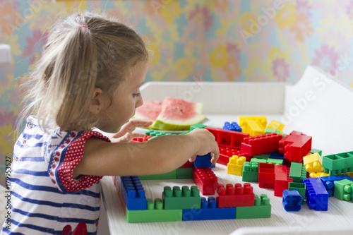 little girl in dress sits at table and collect the colored blocks photo