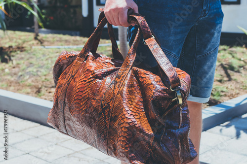 Young handsome man with luxury snakeskin python travel bag. Bali island, Indonesia.
