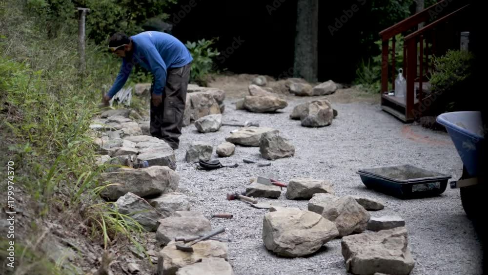 Hardscaper using a stiff brush to dust off the dirt off of the stones he is using to build a stone wall. Hardscaper using a stiff brush to dust off the dirt off of the stones he is using to build a stone wall.