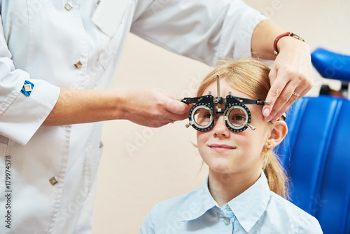 Child optometry concept. Young girl with phoropter during sight testing photo