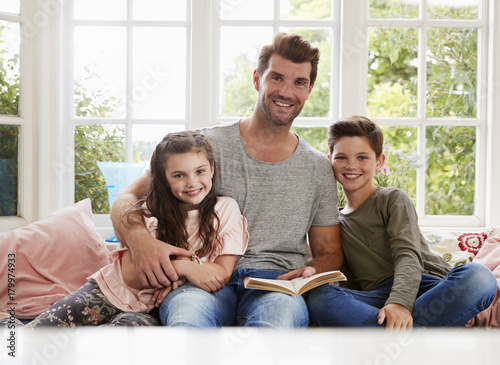 Portrait Of Father Reading Book With Son And Daughter At Home