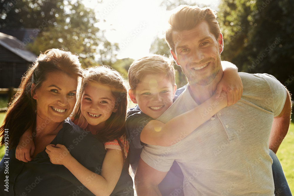 Obraz premium Portrait Of Parents Giving Children Piggyback In Garden