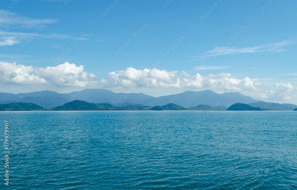 Horizontal of Seascape including Forest Mountain, Blue Sky and Wave of Water Foam in Ocean.