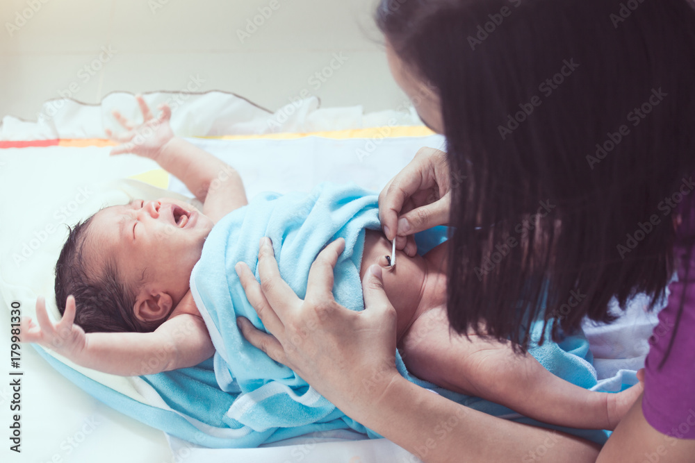 Mother cleaning the navel of asian newborn baby girl with cotton swab
