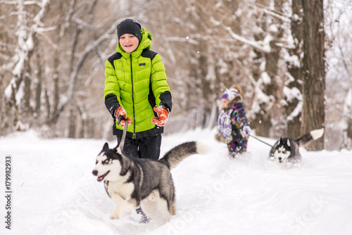 A boy runs after a husky dog in the snow in the park in the winter.