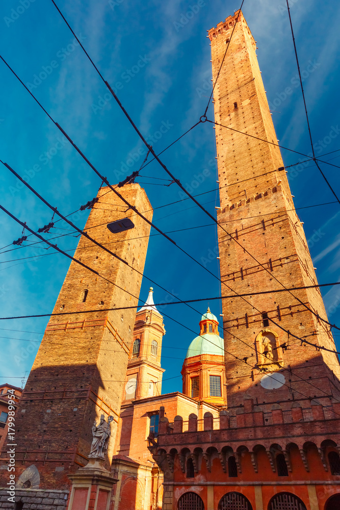 Two Towers, Asinelli and Garisenda, both of them leaning, symbol of Bologna, statue of San Petronius of Bologna and Church of Saints Bartholomew and Gaetano, in the sunny day, Emilia-Romagna, Italy
