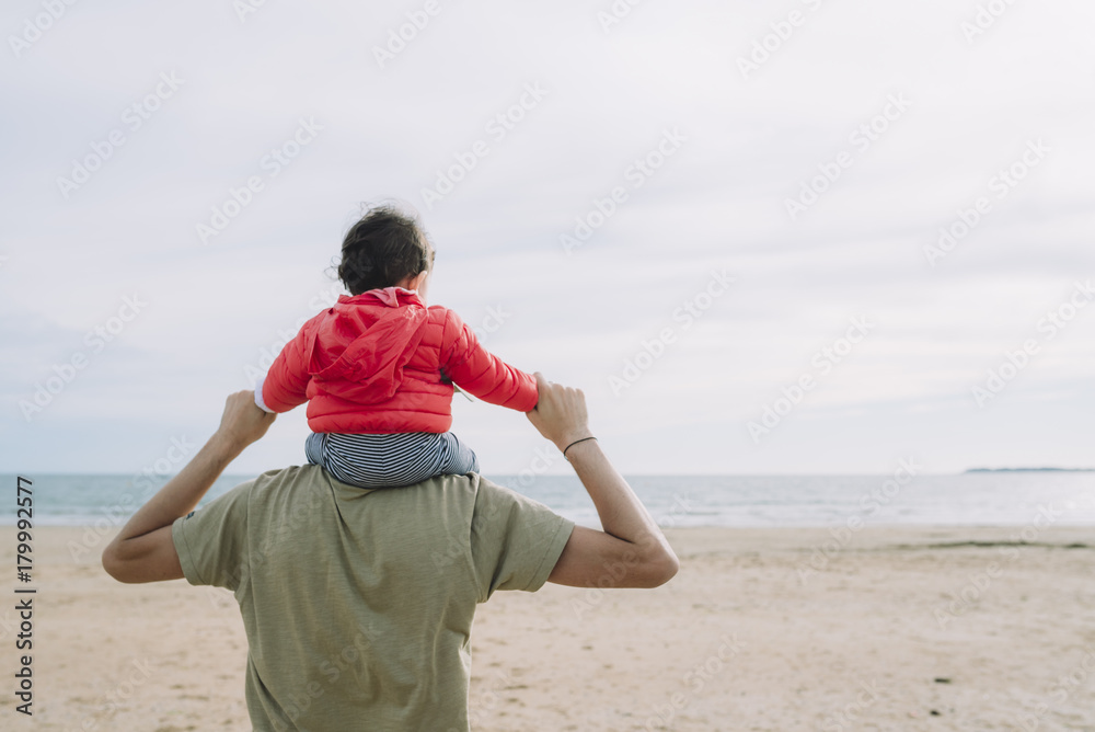 Back view of father carrying his little daughter on shoulders on the beach Back view of father carrying his little daughter on shoulders on the beach
