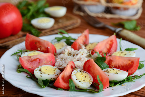 Simple vegetable salad with chicken and eggs. Healthy salad with fresh tomatoes slices, arugula, boiled quail eggs, chicken fillet and spices on a white plate. Rustic style. Closeup