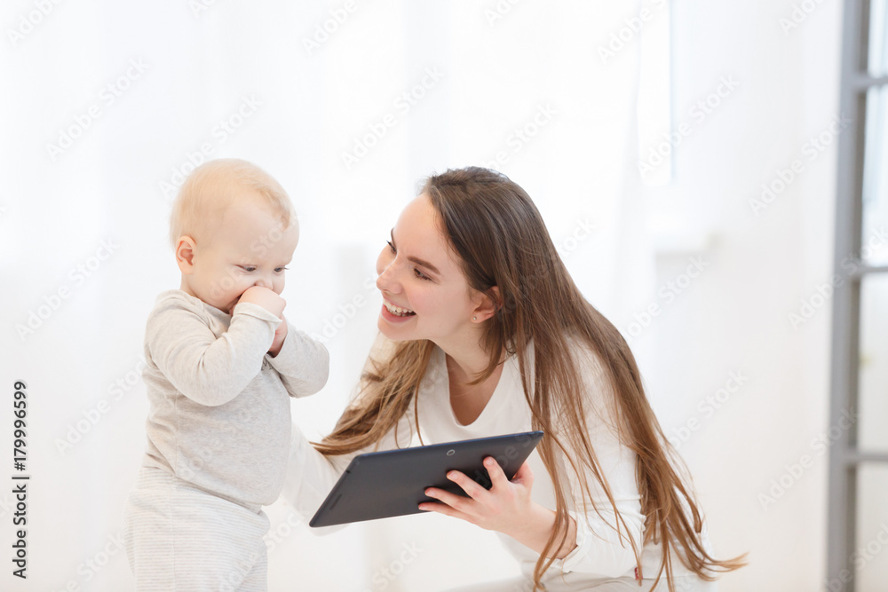 happy young mother plays the tablet with her little baby boy in a light drawing room at home. Education of the child on the tablet, a family portrait happy young mother plays the tablet with her little baby boy in a light drawing room at home. Education of the child on the tablet, a family portrait