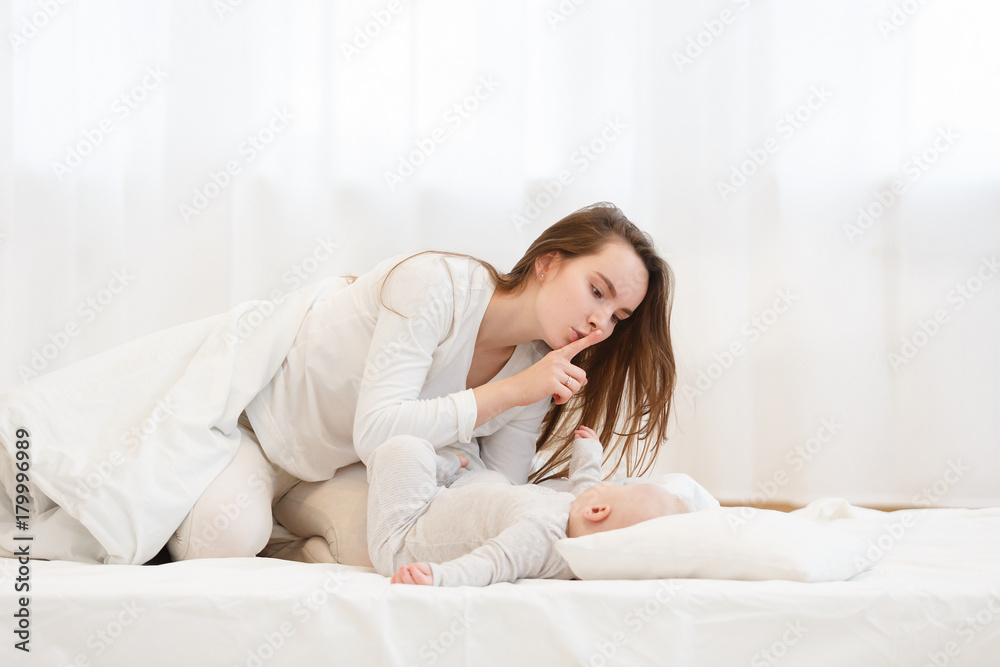 Careful young mother putting down her little baby boy in bed. Happy family. Mother care. Light white domestic interior Careful young mother putting down her little baby boy in bed. Happy family. Mother care. Light white domestic interior