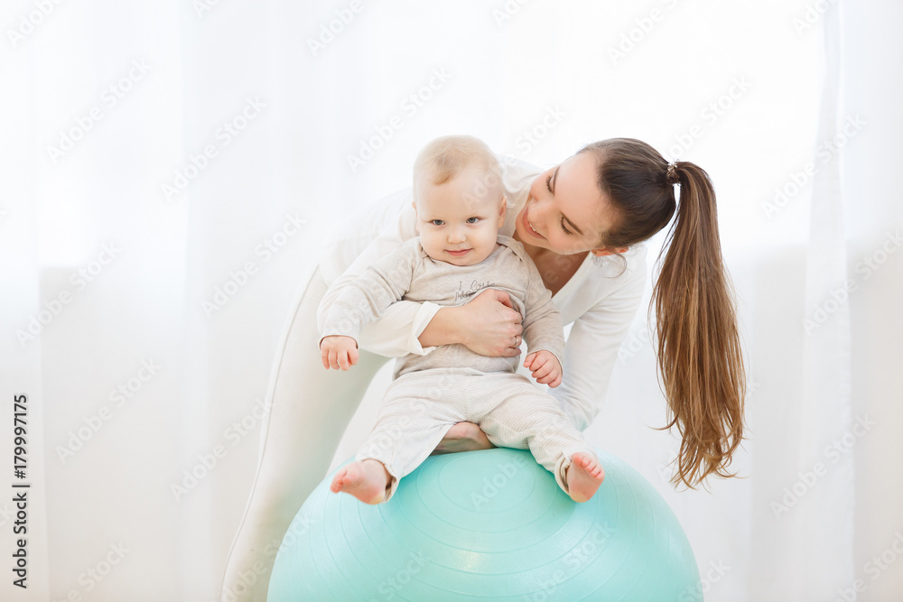 Happy young mother with baby wearing white sport clothes doing gymnastics with Exercise ball and having fun at light domestic home interior. Happy young mother with baby wearing white sport clothes doing gymnastics with Exercise ball and having fun at light domestic home interior.