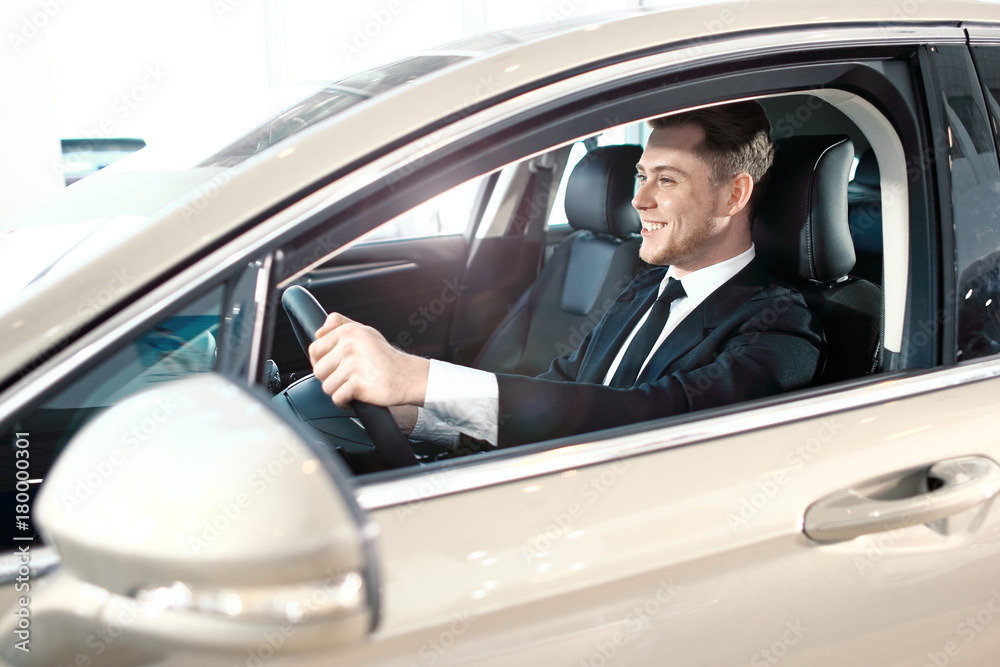 Formal wearing smiling young man behind the wheel.