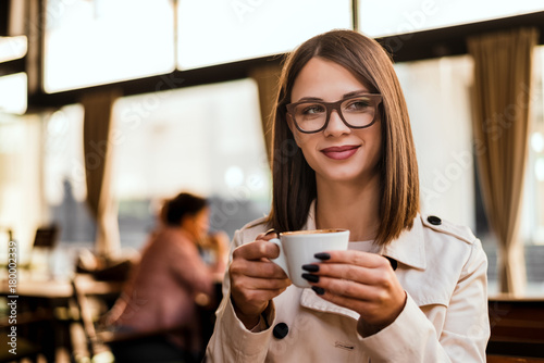 Portrait of brunette woman holding cup of coffee in cafe.